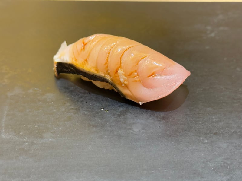 黒いつけ台に、皮を焦がすまで焼いたさわらの握り
