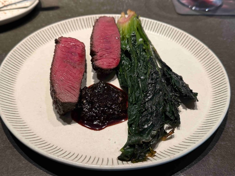 中心が赤く残る鹿肉が二切れ。黒い蕗のとうのソースと、根付きのまま焼いたちぢみほうれん草
