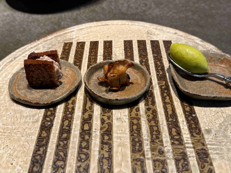 縞模様の板皿に三つの小皿。よもぎのパンデピスにチーズを挟んだもの、揚げたしいたけ、わさび菜のクネル