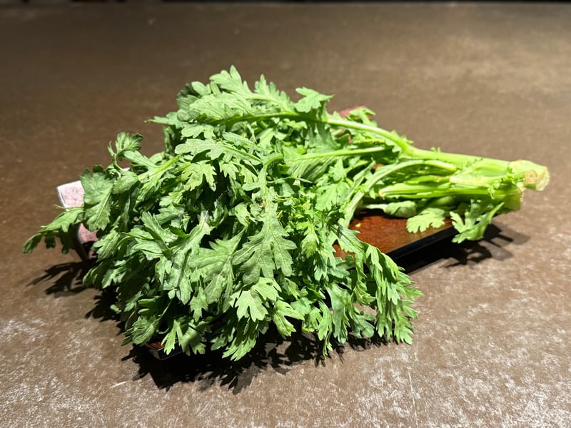 漆の盆に置かれた、茎ごと切った生の春菊の束