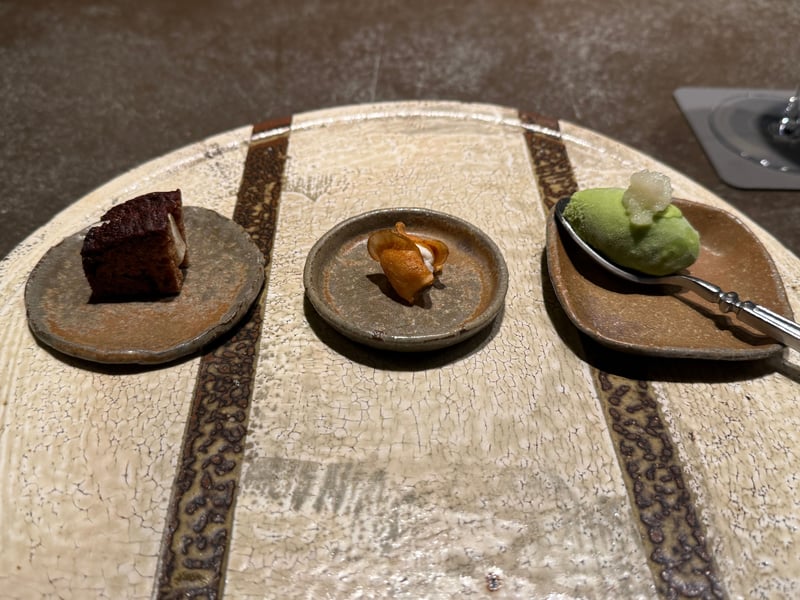丸い陶板に小皿が三つ。茶色いパンデピス、揚げた菊芋のチップ、スプーンにのった緑のアイス
