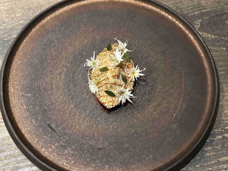茶色の皿に、粉をまとった小さな菓子。白い星形の花と緑の葉がのっている