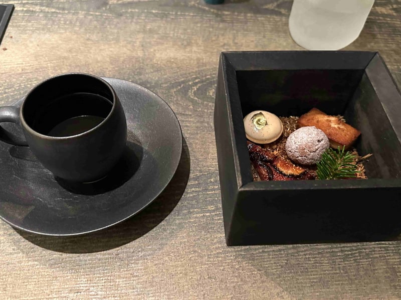 黒い木箱に茶葉を敷いたプティフール。金箔をのせた菓子、粉をまぶした球、フィナンシェ、干したいちじく