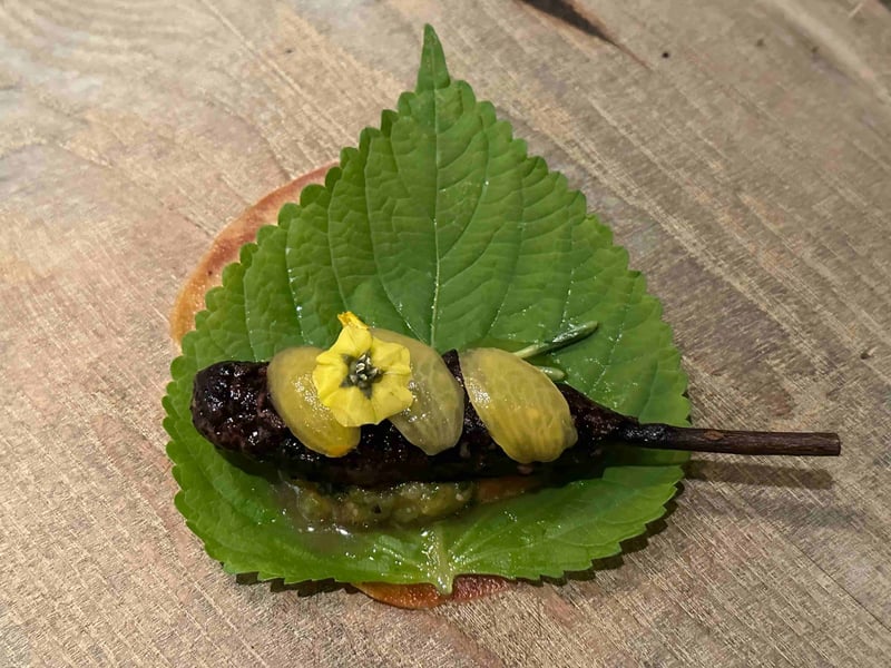 青紫蘇の葉の上に、すっぽんの炭火つくねの串。黄色い花が添えられている