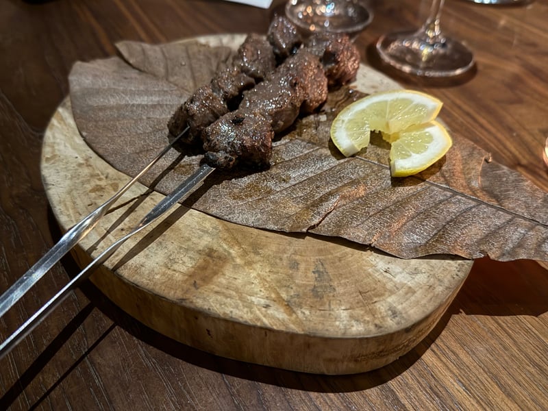 朴葉の上に、薪火で焼いた鹿の串が2本。レモンを2切れ添える