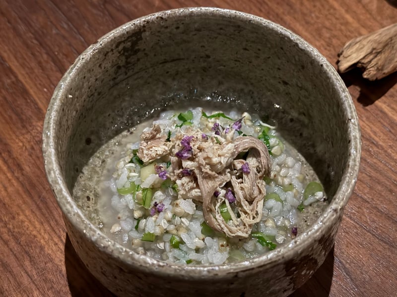 ざらついた器のそば粥に、ほぐした鶏と紫の花