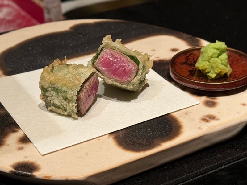 大葉で巻いて揚げた牛肉を二つに切って、断面の赤が見えている。脇に山葵