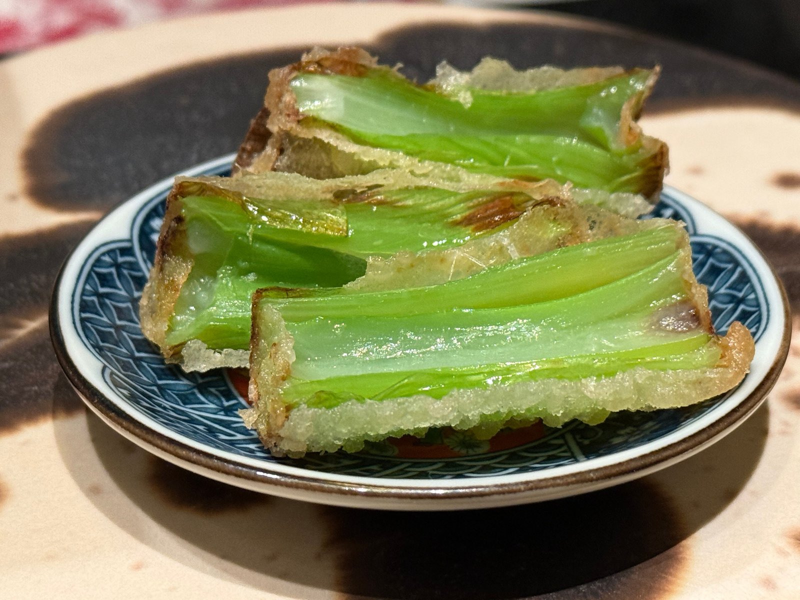 染付の皿に九条ネギの原種の天麩羅が三切れ、衣の中で緑の茎が透けている
