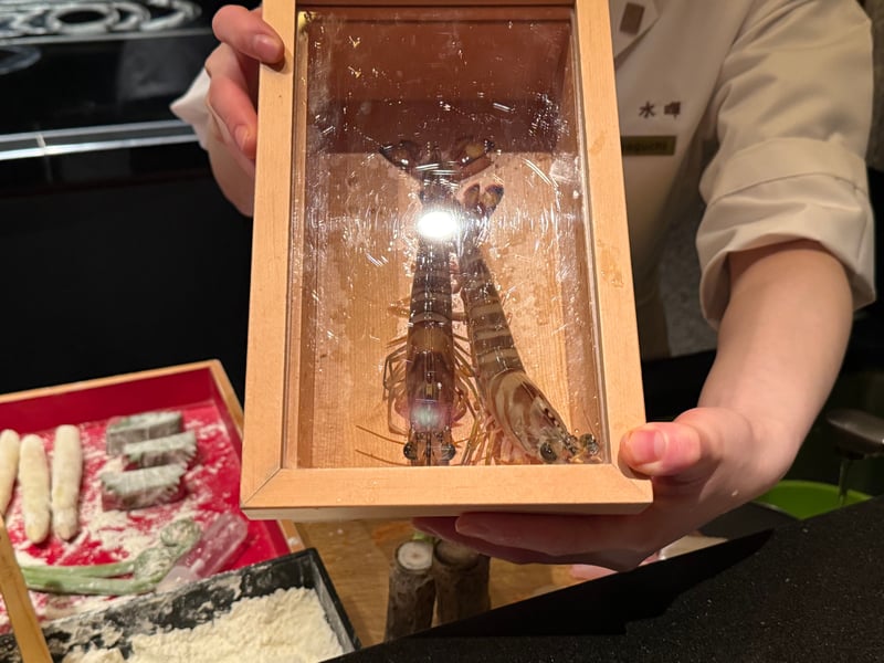 ガラス蓋の木箱に入った生きた車海老が二尾。店の人が持っている