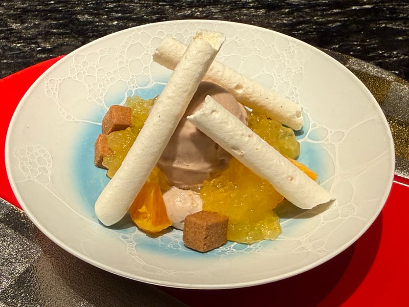 白い鉢に盛ったアイスと黄色いジュレ、柑橘、薄く巻いた焼き菓子