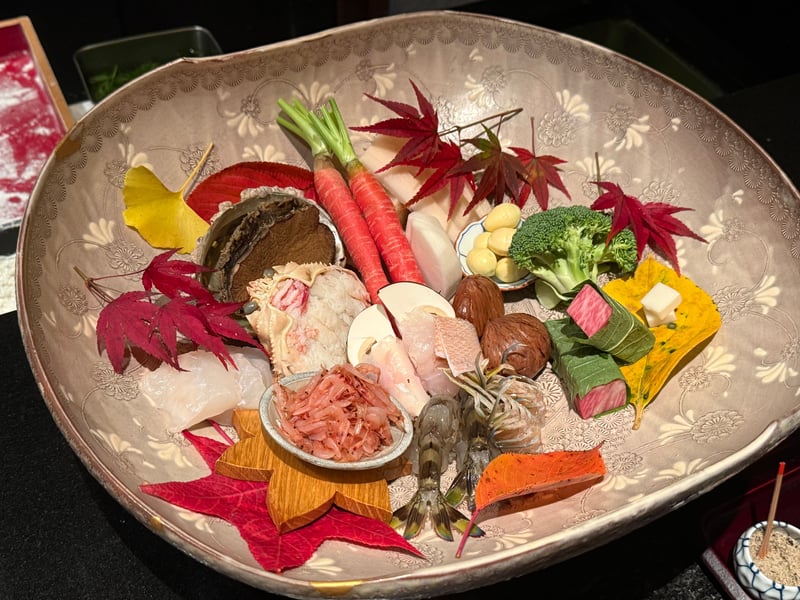 紅葉と銀杏の葉を敷いた大鉢に並べたこの日の食材。鮑、セイコ蟹、人参、蓮根、銀杏、ブロッコリー、車海老、桜海老、白身魚、松茸、栗、大葉で巻いた牛肉