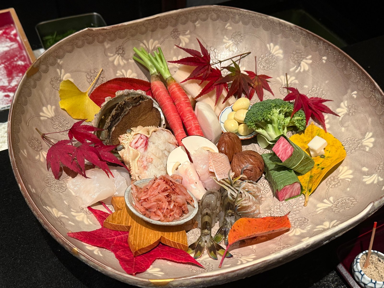 紅葉と銀杏の葉を敷いた大鉢に並べたこの日の食材。鮑、セイコ蟹、人参、蓮根、銀杏、ブロッコリー、車海老、桜海老、白身魚、松茸、栗、大葉で巻いた牛肉