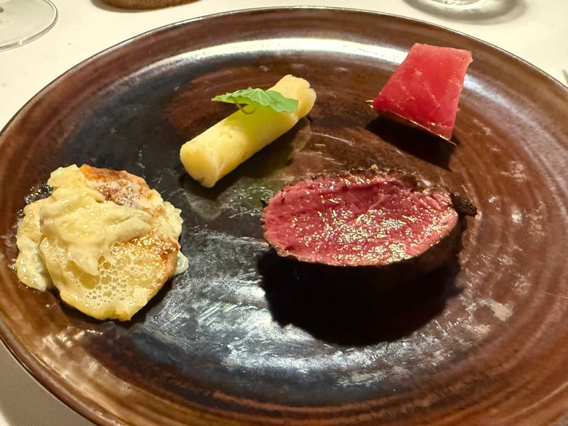飴色の焼き締めの皿に、炭火で焼いた蝦夷鹿の厚い輪切り。横に黄色いピュレの円筒と紅色のリンゴのコンポート