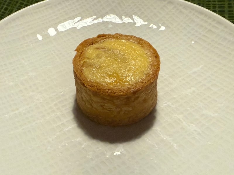 白い皿に置かれた、円筒形のパイ生地に玉葱の詰め物を焼き込んだ小さなタルト