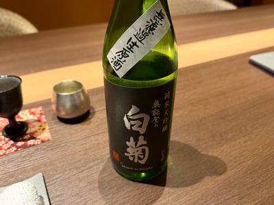 奥能登の白菊 純米大吟醸の緑瓶。首に手書きの短冊、横に錫と黒の猪口