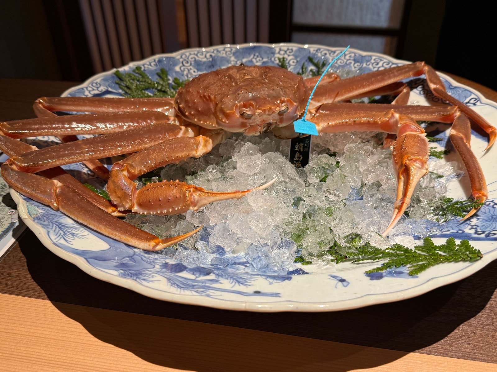 氷と杉の葉を敷いた染付の大皿に、石川県蛸島の荷札を付けたズワイ蟹が一杯