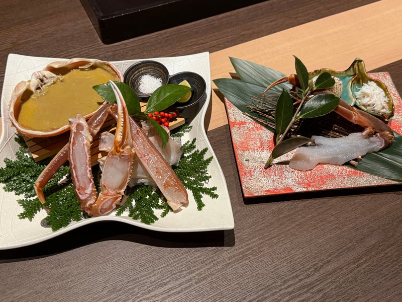 白い皿に生の加能蟹の脚と、甲羅いっぱいの蟹味噌、塩とすだち。右の板に生の身とほぐした蟹の身