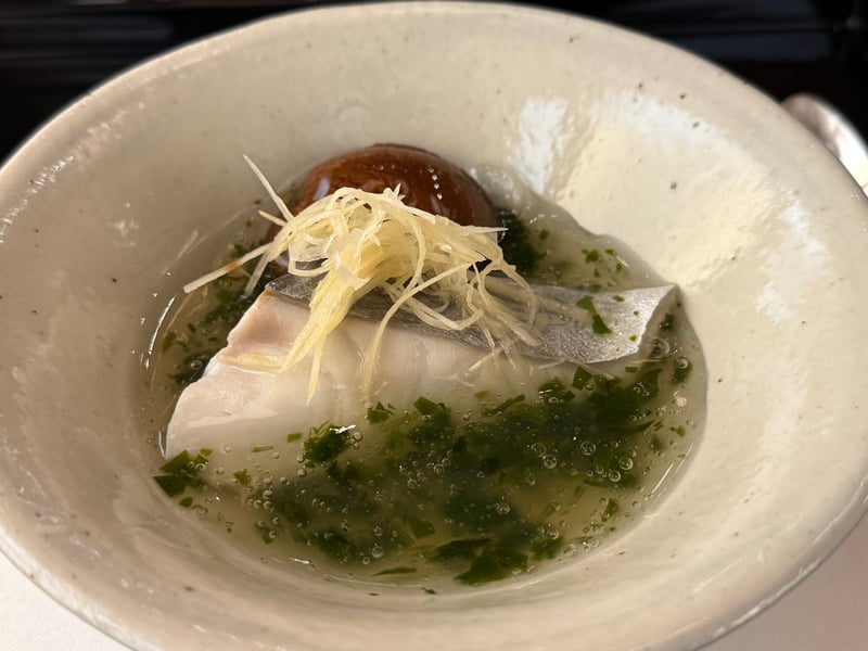 白い鉢のさわらに若布のあん。椎茸と針生姜を載せる