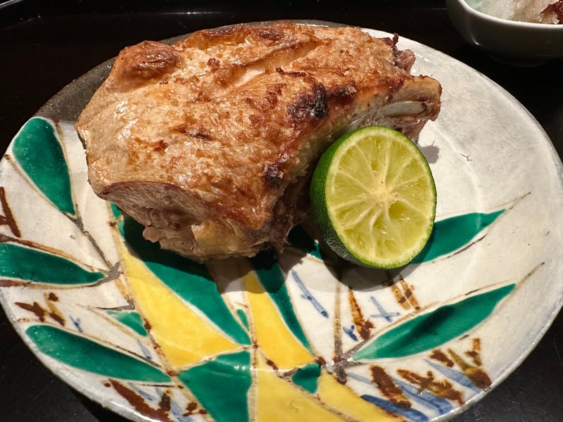九谷風の緑と黄の皿に、皮を香ばしく焼いた骨付きの身。半割りの酢橘が添えられている