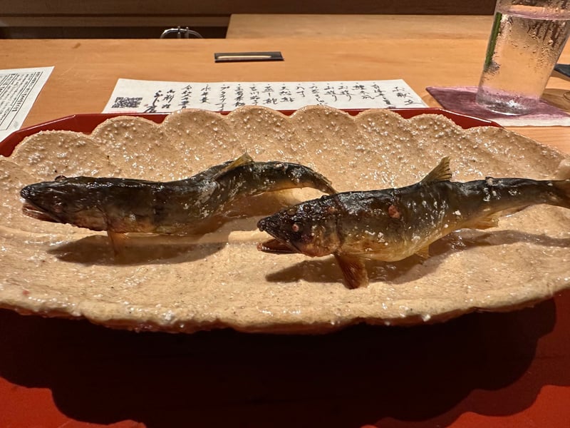 波形の皿に炭火で焼いた天然鮎が二尾。奥に手書きのお献立が置かれている