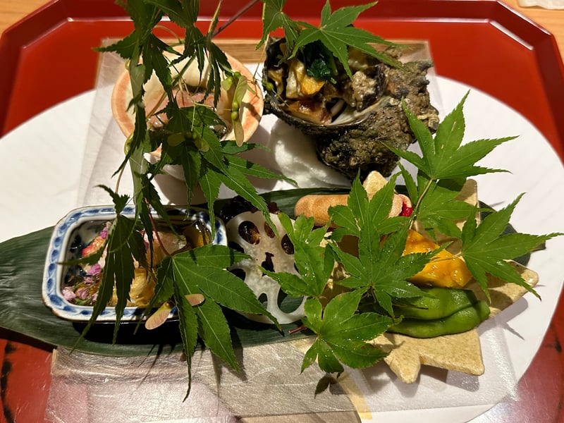 朱塗りの盆に並ぶ八寸。サザエの殻、蓮根、最中、小鉢が紅葉の枝とともに配してある