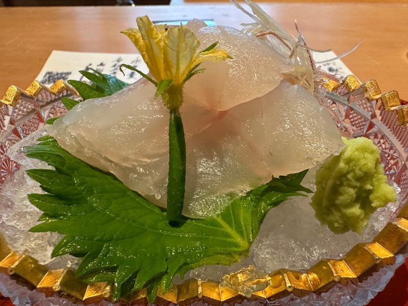金縁の切子に氷を敷き、キジハタの薄造り。大葉と黄色い花、みょうがが添えられている