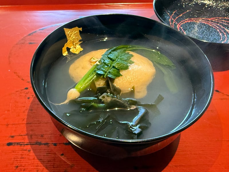 黒の椀に蛤しんじょう、若布と鶯菜、金箔と三つ葉