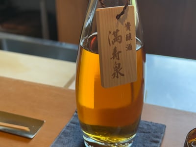 琥珀色の貴醸酒を注いだガラスの器。満寿泉 貴醸酒の木札が下がる