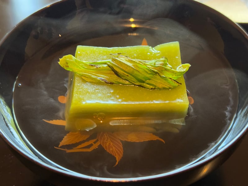 黒漆の椀に沈めた緑の豌豆豆富。上に炙った蕗のとうの葉