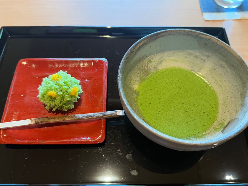 朱の角皿に緑の菜の花きんとん。黄色の粒を散らし、黒文字を添えて抹茶と並ぶ