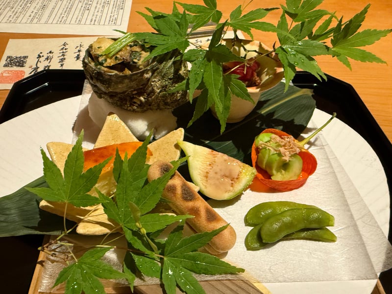 黒い盆に青楓を散らした八寸。さざえの殻、もなか、白いちじく、枝豆が並ぶ