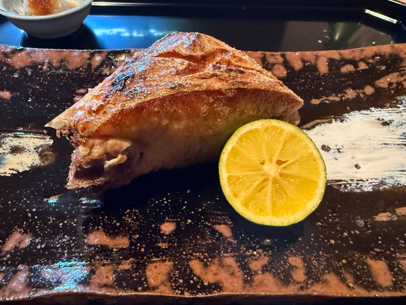 黒い長皿にのったぶりの塩焼きと半割りの柑橘