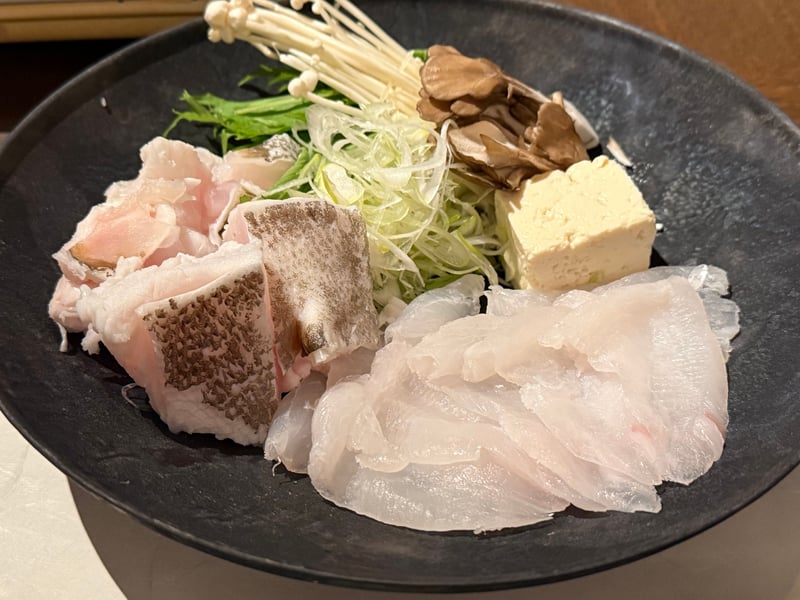 黒い皿に、薄く引いた九絵の身と皮付きのアラの塊。水菜、えのき、舞茸、白髪ねぎ、豆腐