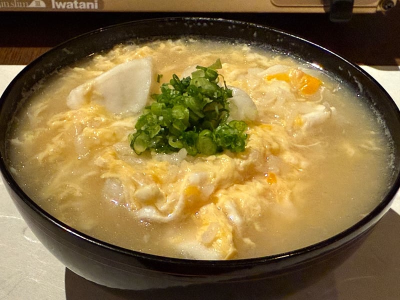黒い椀に、卵でとじたアラ雑炊。大根と青ねぎを載せる