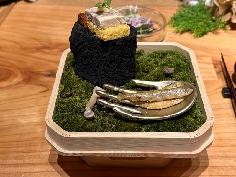 苔を敷いた木箱に、炭のような黒い台にのせたブリオッシュと信玄鶏のプレッセ、匙にのせたワカサギ