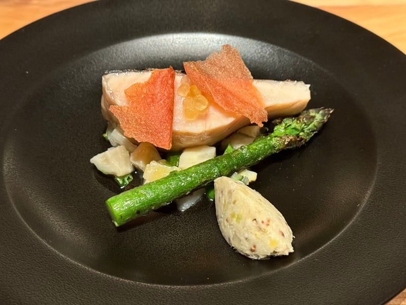 黒い皿にのせた岩魚の炭火焼き。薄いオレンジのチップ、焼いたアスパラガス、筍、いものクネル