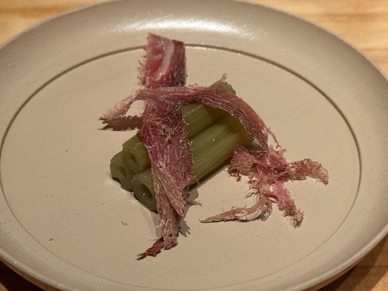 灰色の平皿に、淡い緑の茎を並べて薄く削った鹿節をかぶせた口休め