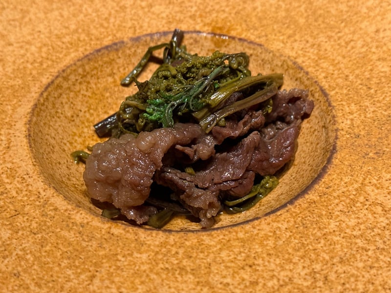 浅い鉢に盛った熊のもも肉のすき焼き風と、わらび