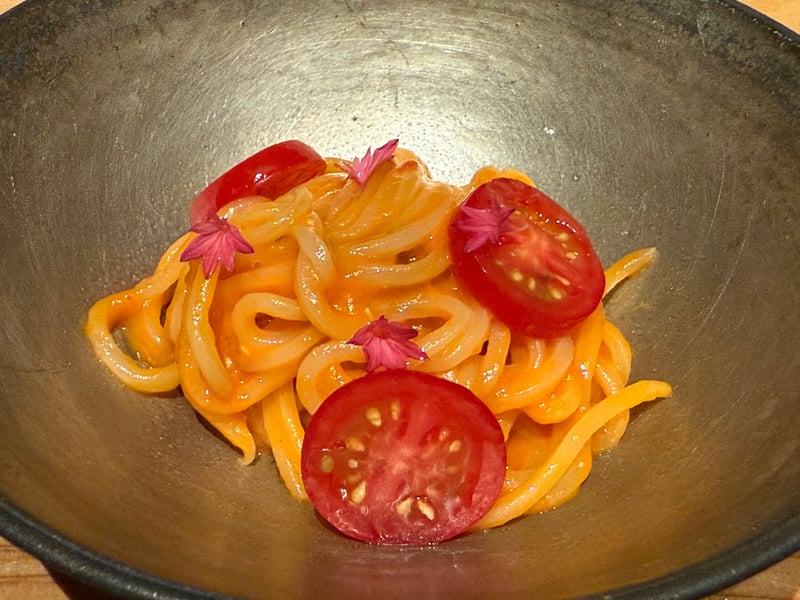 黒い鉢に盛った太めのパスタ。ミニトマトの輪切りと花を散らしてある