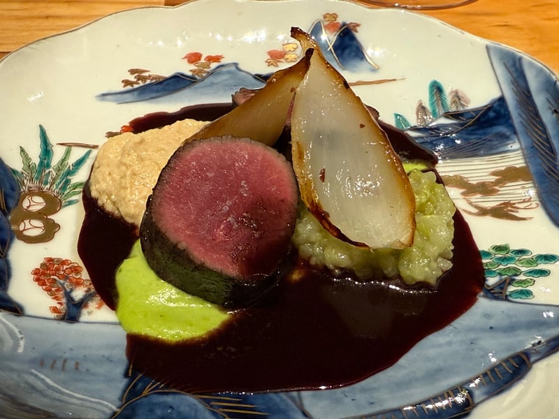 染付の皿に、赤ワインのソースを敷いた鹿のロースト。あけぼの大豆のフムス、ピーマンのピュレ、焼いた玉ねぎ