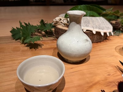 白い徳利と盃に注いだ日本酒。奥に猪の頭骨が置いてある