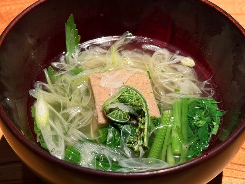 黒い椀に張られた澄んだ出汁。胡桃豆腐、こごみ、うるい、あさつきが浮かんでいる
