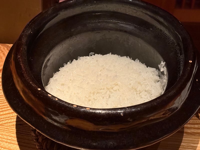 黒い土鍋の蓋を取ったところ。粒の立った白飯が炊き上がっている