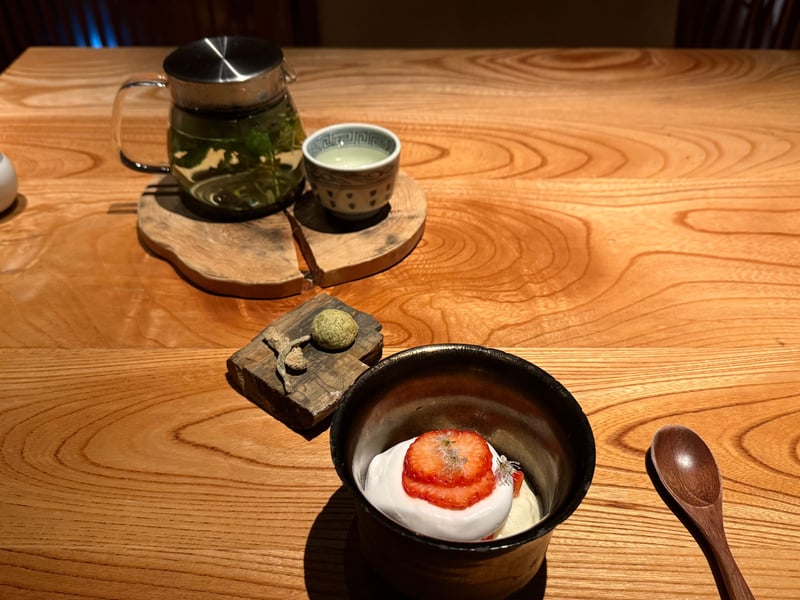 黒い器に盛った白いムースと苺、白い花。横によもぎの菓子とハーブティーのポット