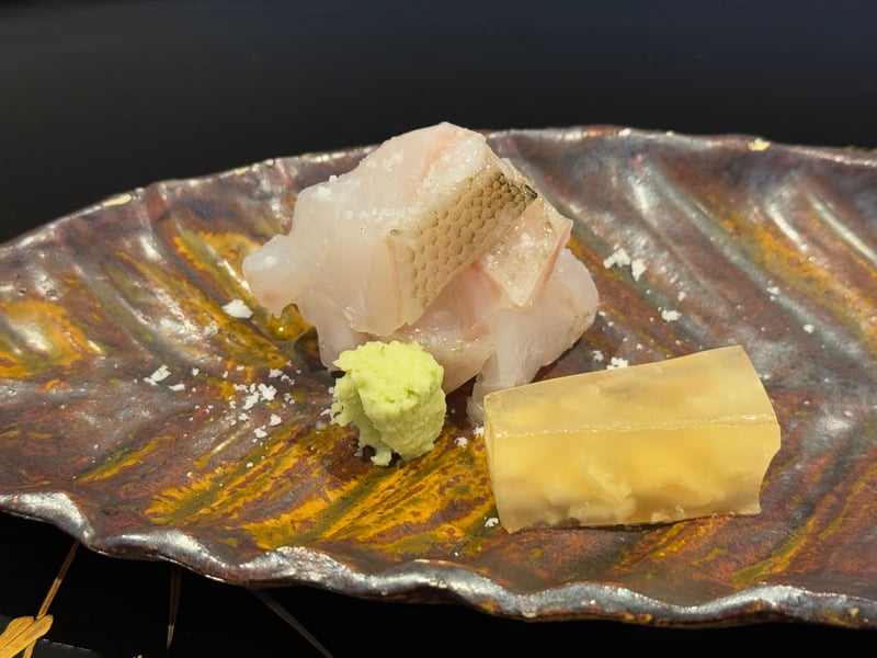 飴釉の葉形の皿に、皮を炙ったクエの薄造りと山葵、琥珀色の煮凝り