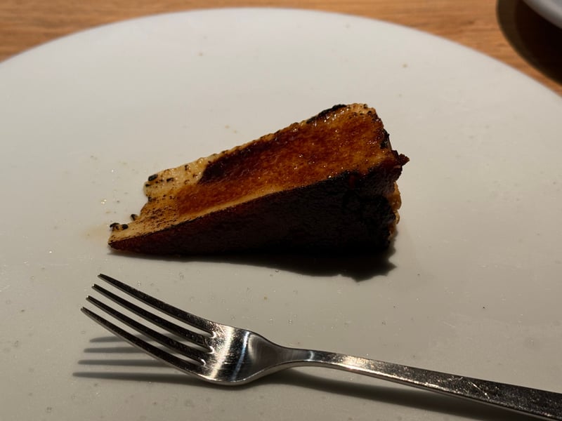 白い皿に、表面を黒く焼いたバスクチーズケーキが一切れ。手前にフォーク