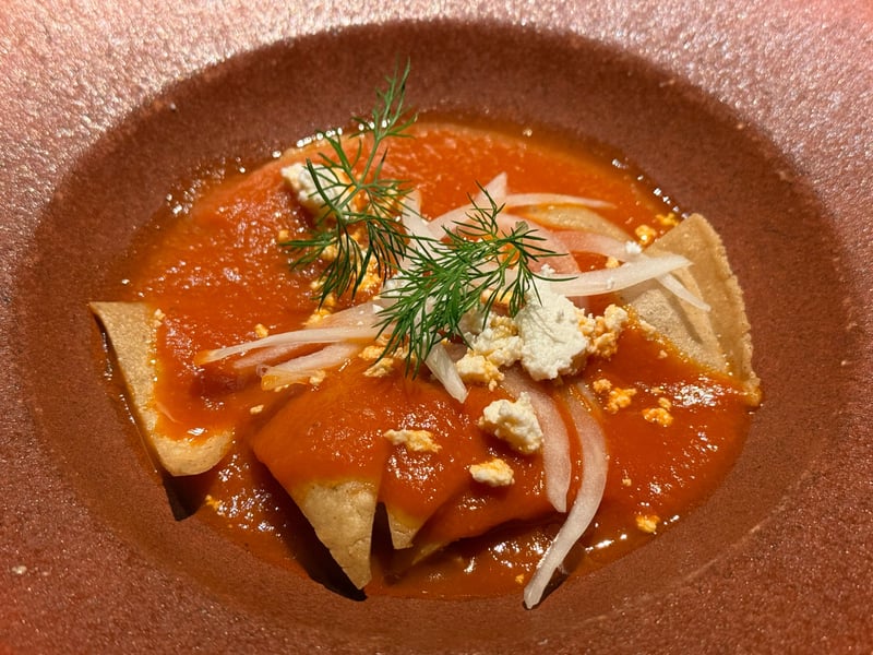 赤茶の鉢に、トマトソースで煮たとうもろこしのトルティーヤ。崩したフレッシュチーズ、薄切りの白玉ねぎ、ディルを載せる