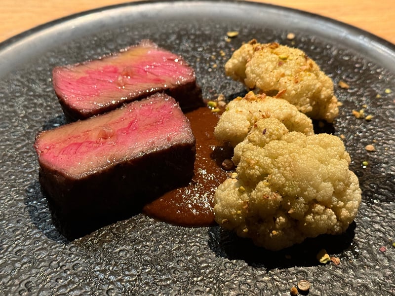 黒い皿に、ロゼ色に焼いた牛モモ肉が2切れ。茶色いモレソースと、ピスタチオをまぶしたカリフラワーの素揚げが3つ