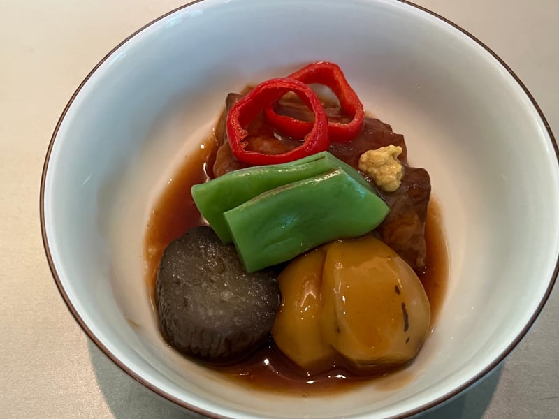 白い小鉢のキビまる豚の角煮。赤唐辛子の輪切りと青味、京茄子、栗、マスタードが添えられている