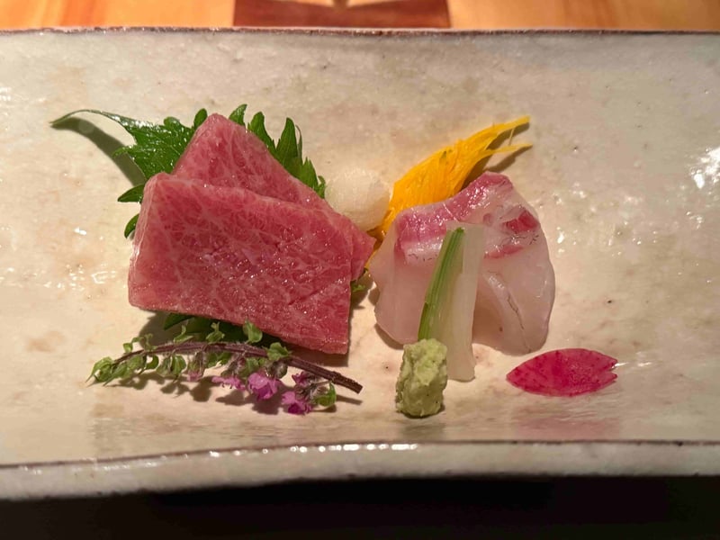 白い長皿の造里。霜降りの鮪二切れと鯛。穂紫蘇、菊の花びら、わさびが添えられている